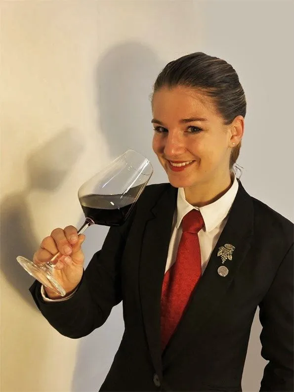 Audrey Brugière, en tenue de sommelière, hume un verre de vin rouge.